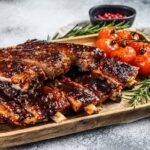 Delicious barbecued ribs seasoned with a spicy basting sauce and served with baked tomatoes. Gray background. Top view.