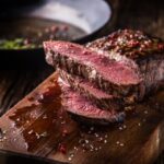 Beef steak. Juicy medium Rib Eye steak slices on wooden board with fork and knife herbs spices and salt.